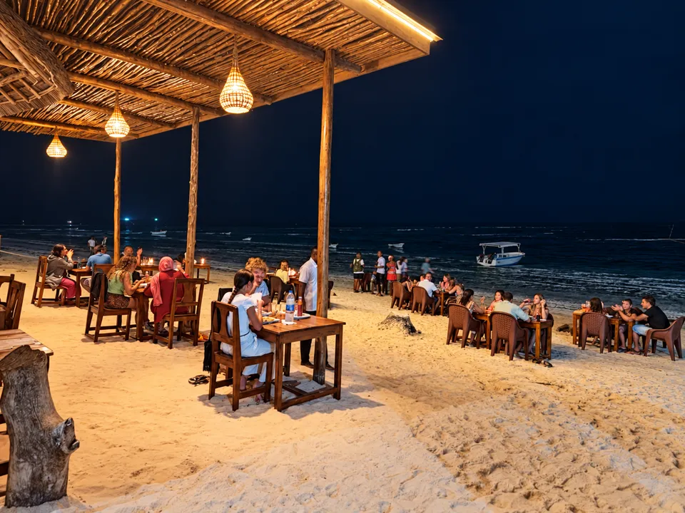 Tables on the sand under warm lanterns at night